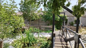 A wooden deck over a pond with surrounding greenery and a stone wall in the background. - Large, single-story, air-conditioned house with 5 bedrooms near the Marais Poitevin (Saint-Pierre-d'Amilly)