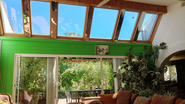 A room with a green wall, a large sliding glass door leading to an outdoor area, a sofa with cushions, and a table. - Large, single-story, air-conditioned house with 5 bedrooms near the Marais Poitevin (Saint-Pierre-d'Amilly)