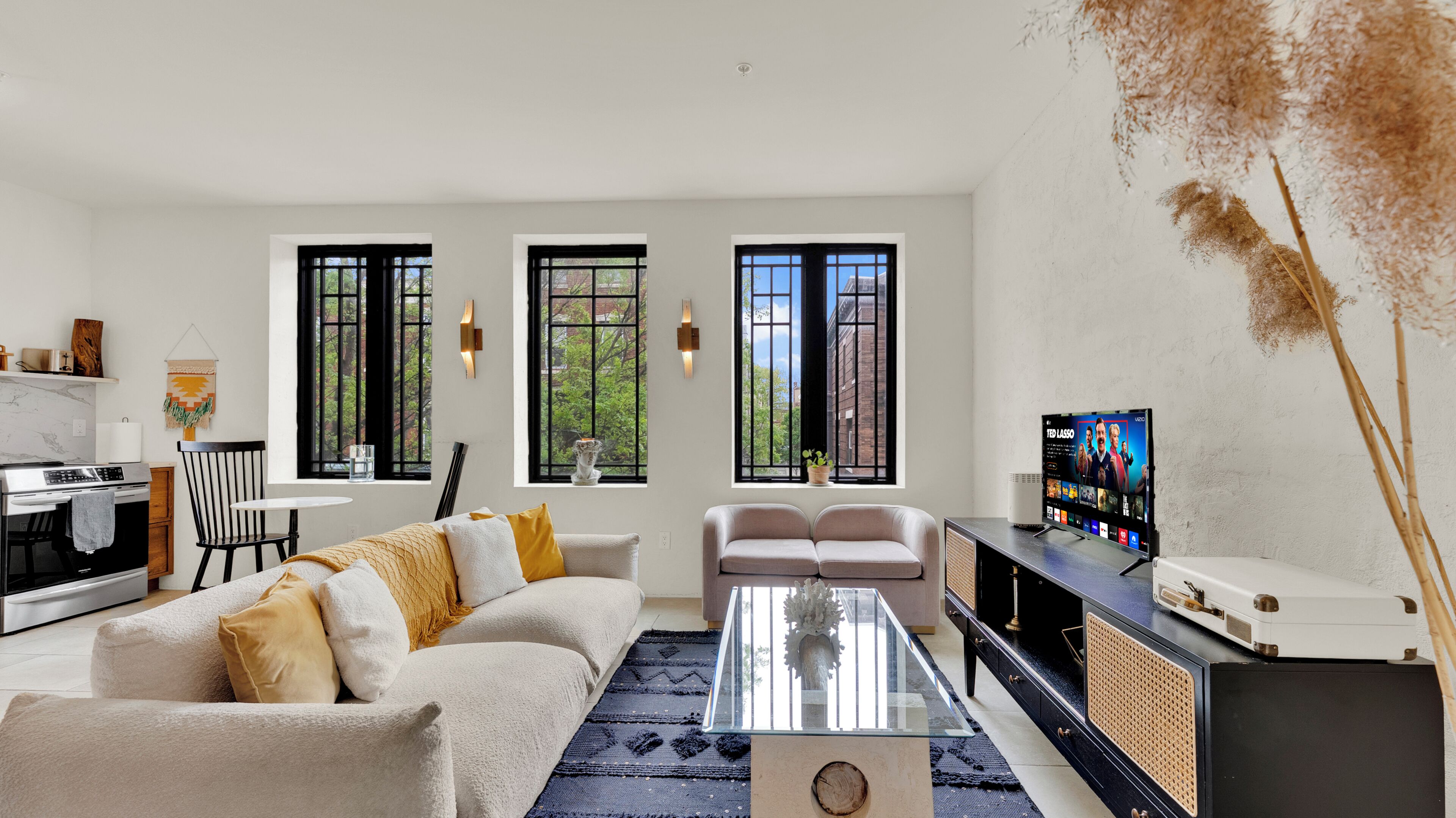 Ein modernes Wohnzimmer mit Sofa, Couchtisch, Fernseher und Küchenzeile mit Herd und Schränken.