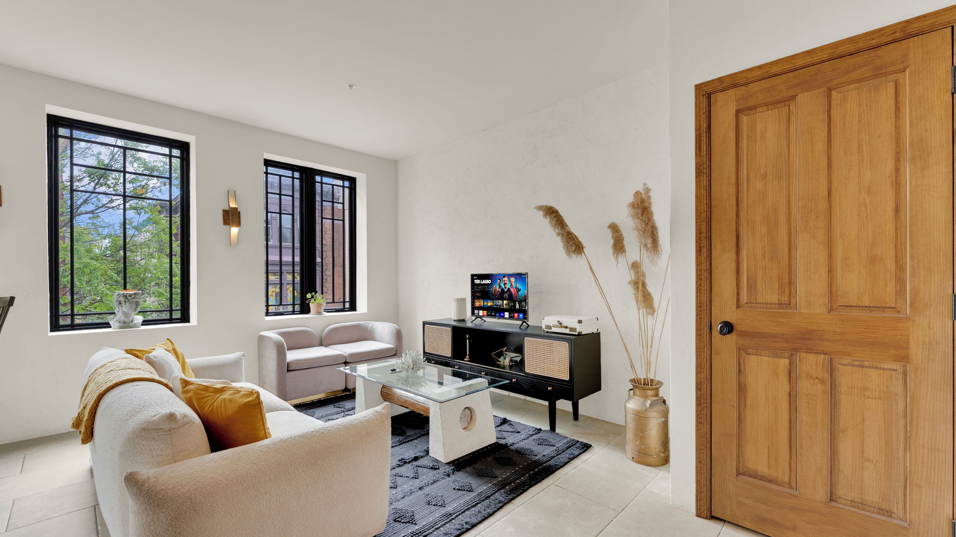 Sala de estar com sofá, mesa de centro, televisão e plantas decorativas.