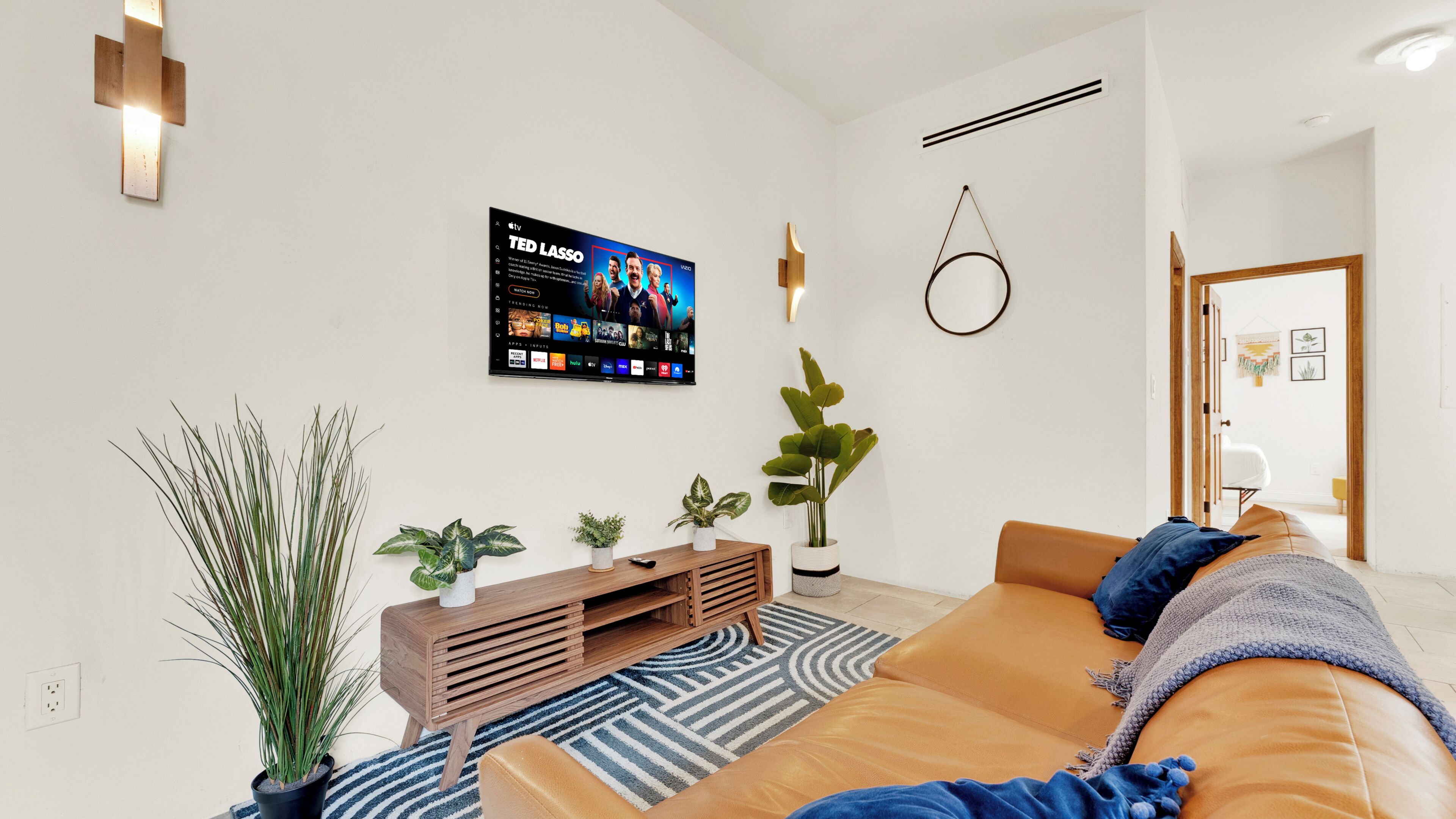 Uma sala de estar moderna com televisão, sofá, plantas e um console de madeira.