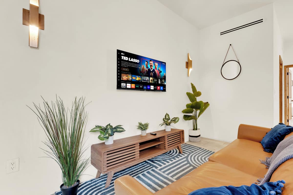A modern living room with a TV, sofa, plants, and a wooden console.