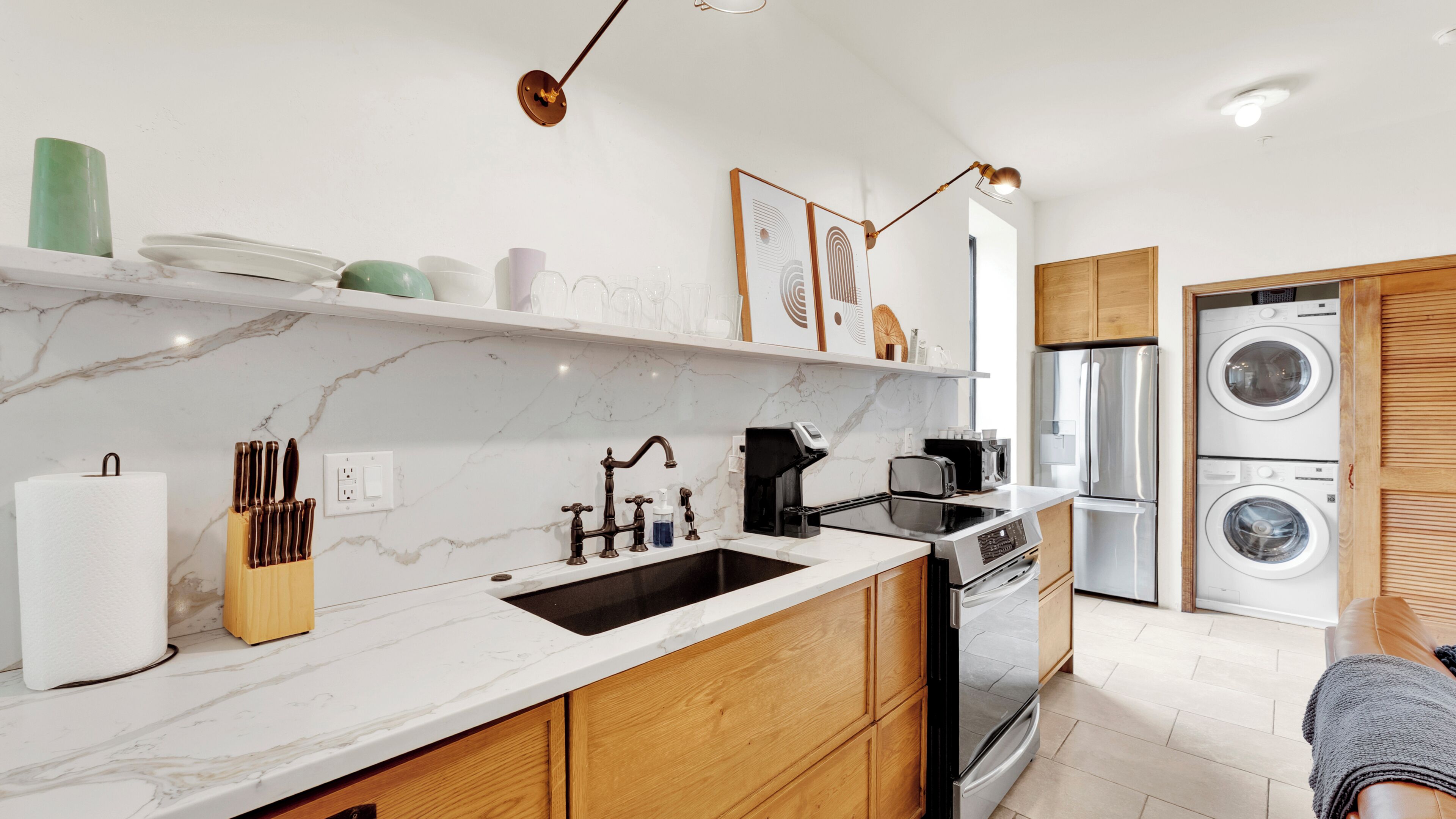 A modern kitchen with a marble countertop, wooden cabinets, a sink, a coffee maker, and a built-in washing machine.