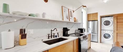 A modern kitchen with a marble countertop, wooden cabinets, a sink, a coffee maker, and a built-in washing machine.