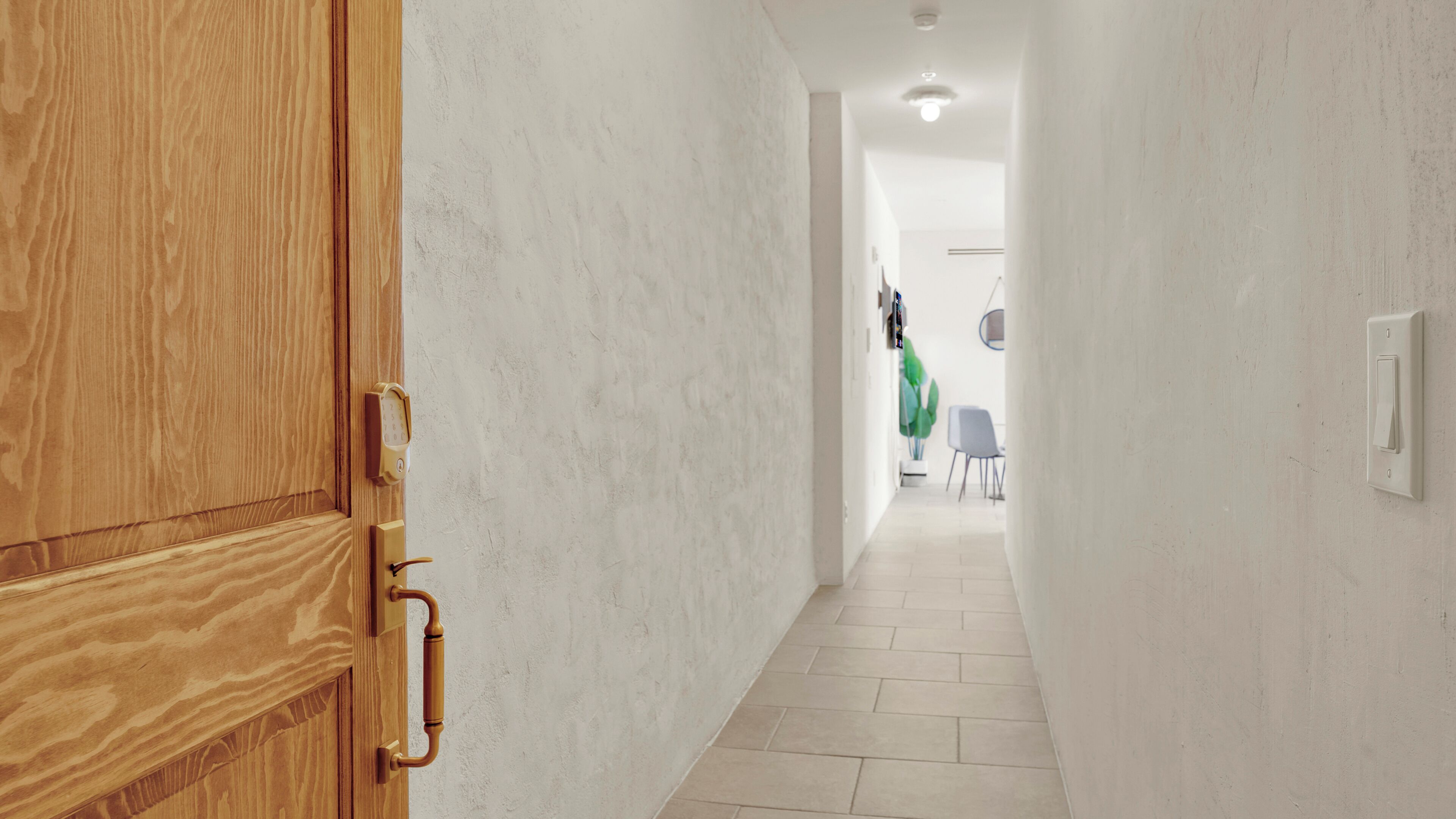 A hallway with a wooden door, a light switch, and a tiled floor.