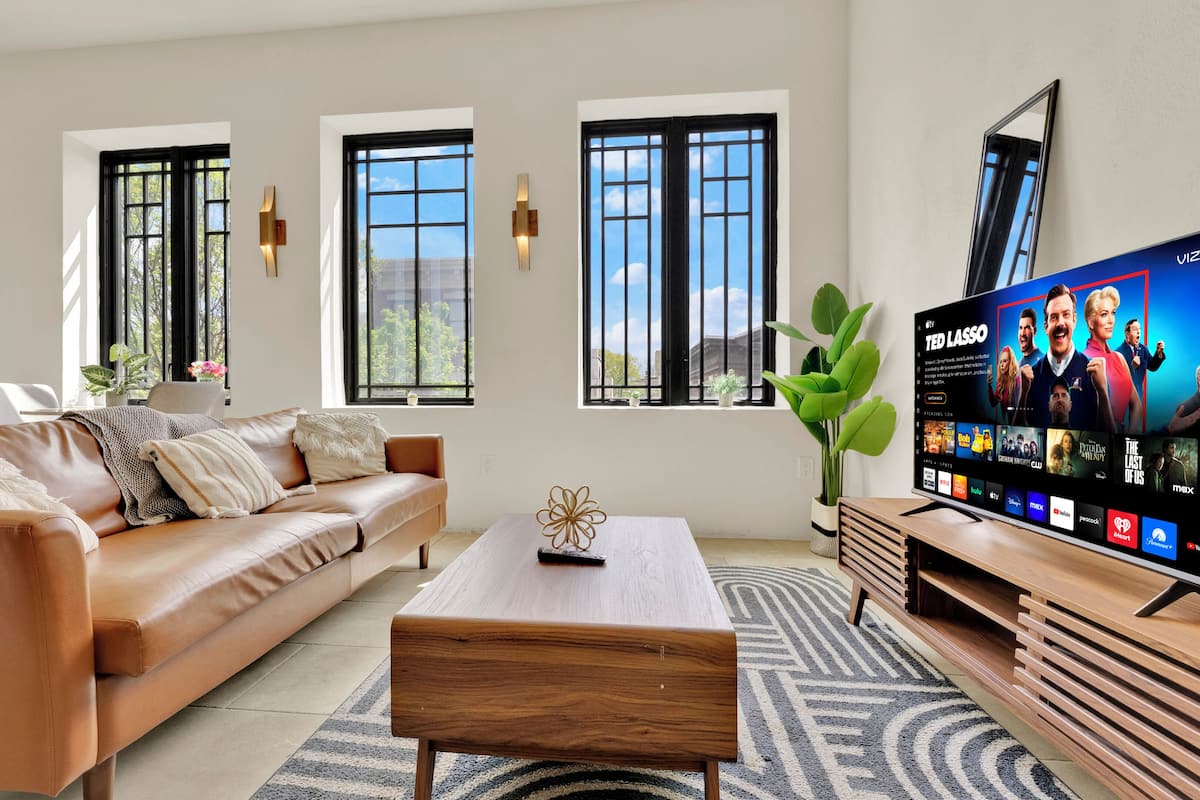 A modern living room with a leather sofa, a wooden coffee table, and a flat-screen TV displaying a show.
