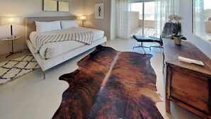 A bedroom with a bed, a desk, a chair, a large rug, and a window with curtains.