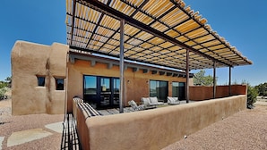 A modern house with a covered patio, outdoor seating, and a view of the desert landscape.