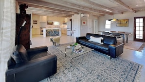 A spacious living room with a black leather sofa, a glass coffee table, and a patterned rug.