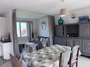 A dining area with a table, chairs, and a view through a window. - Villa Jo - Family Home in Grand-Village (Le Grand-Village-Plage)