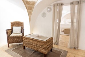 Ein Korbstuhl mit Kissen, ein kleiner Tisch mit Kerze und Blick auf einen Raum mit Vorhängen und einem Bett.