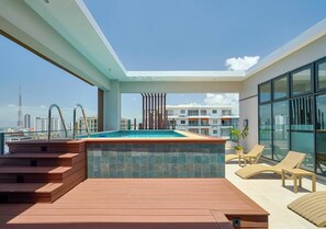 A rooftop pool with a city view, a wooden deck, and lounge chairs. - ®{2BR | Urban~Oasis} DowntownSD +Pool+Gym+Balcony (Santo Domingo)