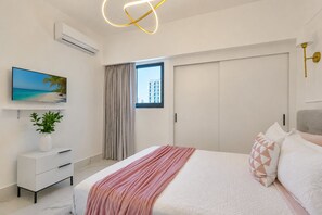 Ein modernes Schlafzimmer mit Bett, Fernseher, Pflanze, Fenster mit Vorhängen und Blick auf Gebäude.