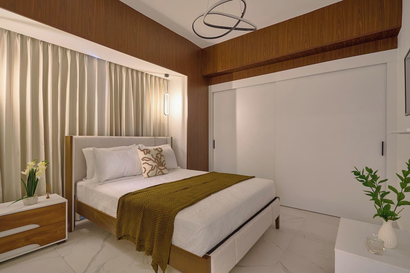 Een moderne slaapkamer met een bed, nachtkastje, gordijnen en een kledingkast.