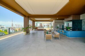 Ein geräumiger Balkon mit Blick auf die Stadt, eine Sitzecke mit Sesseln und einer Couch sowie eine Küchenzeile mit Arbeitsplatte und Stühlen.