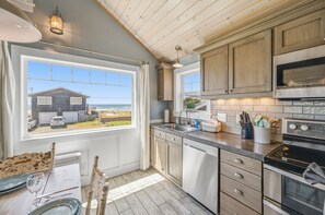 A kitchen with wooden cabinets, a stainless steel oven, and a view of a house through a window.