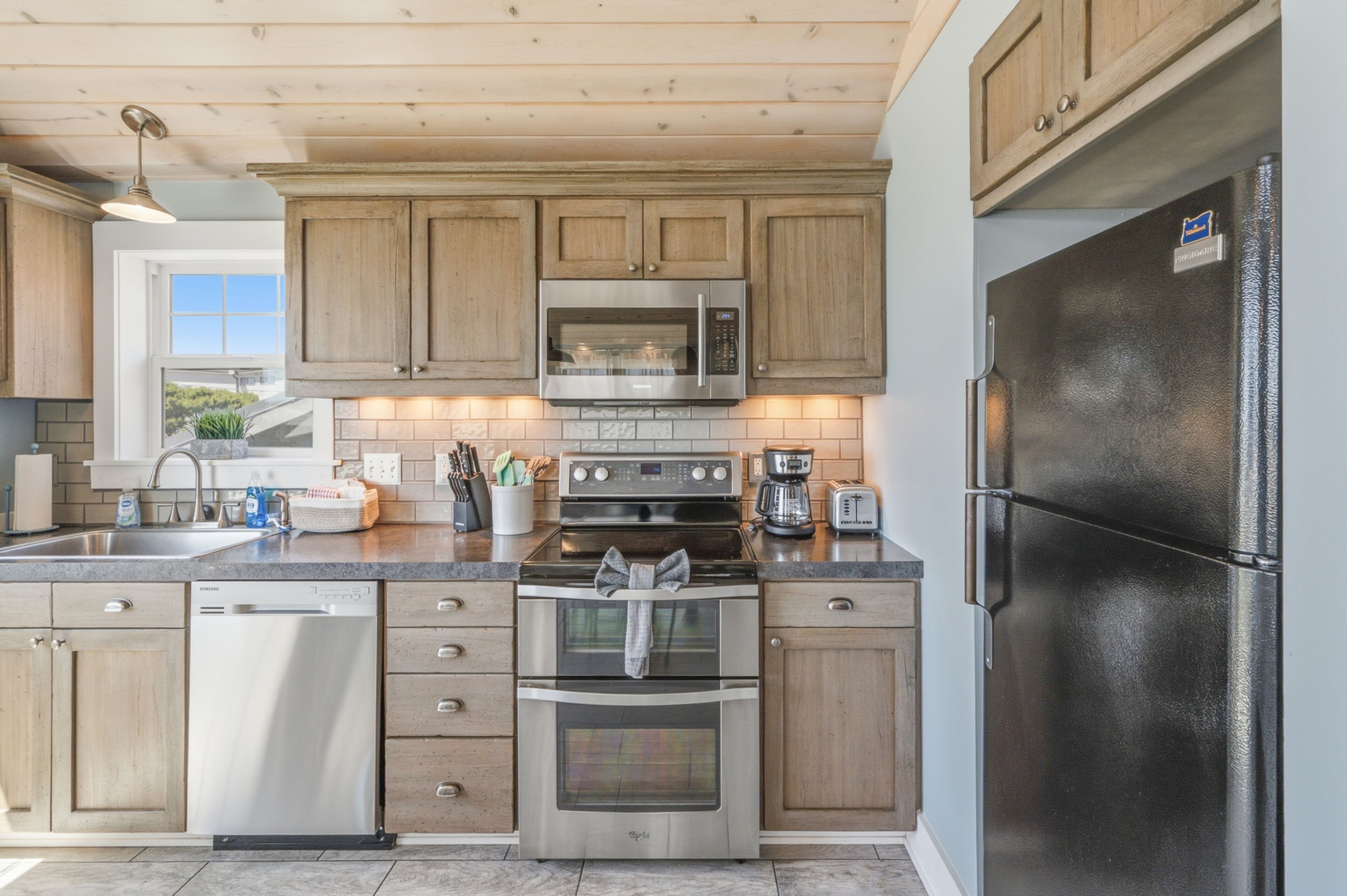 A kitchen with wooden cabinets, stainless steel appliances, and a view to the outside.