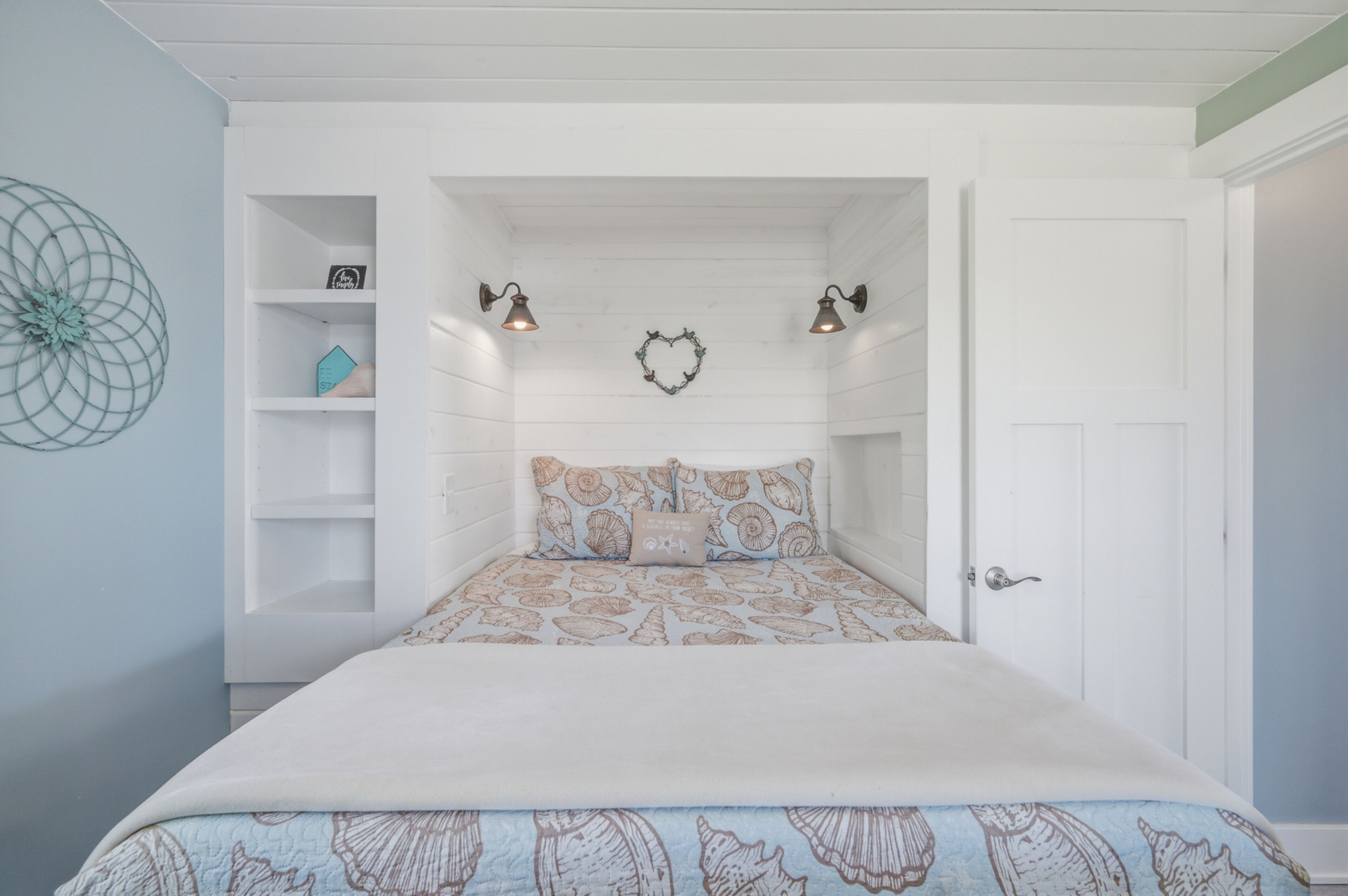 A bedroom with a bed, two wall-mounted lights, a heart-shaped decoration, and a door.