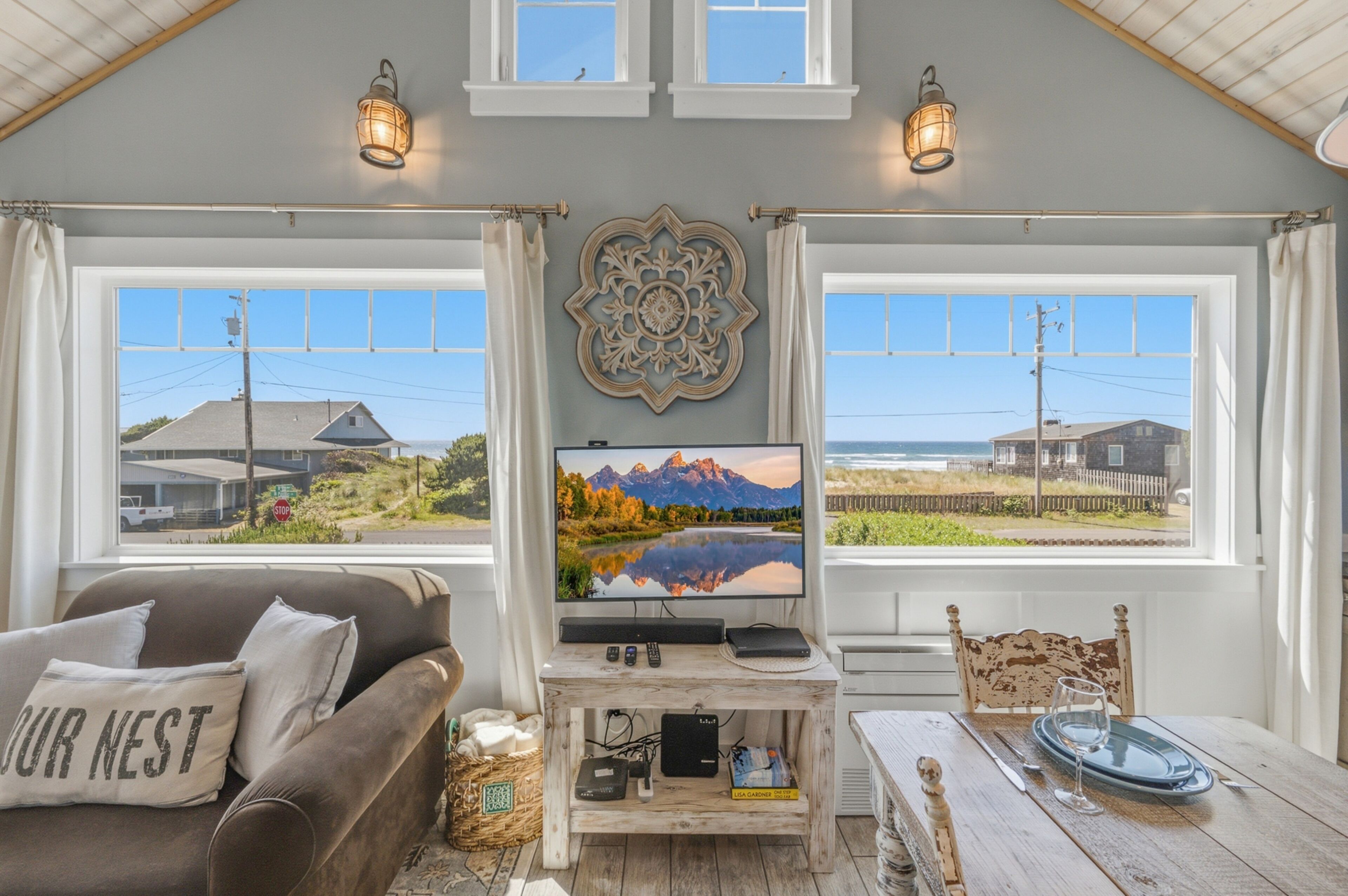 A cozy room with a TV, a wooden table, and a view of mountains through large windows.