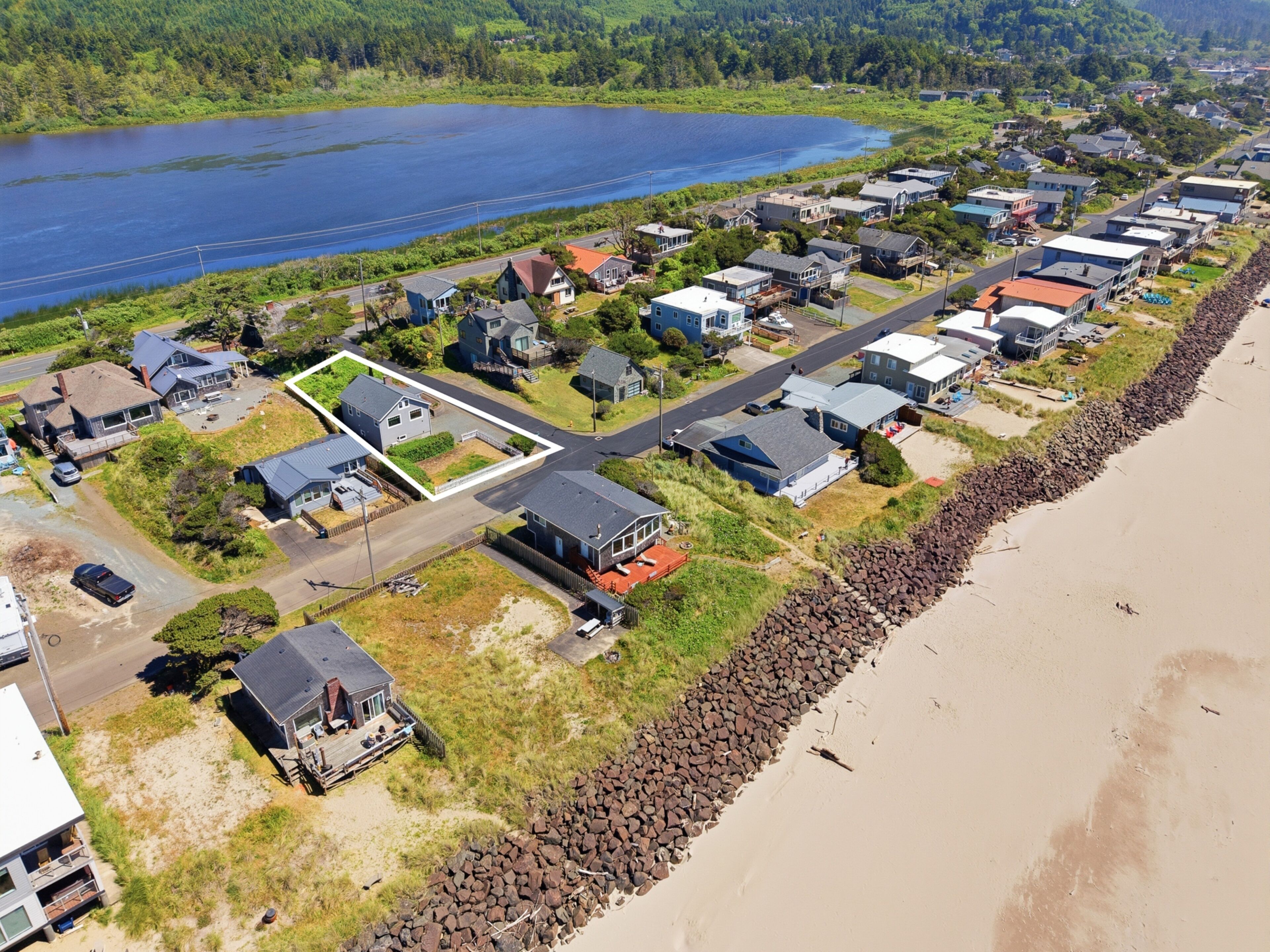An aerial view of a coastal residential area with houses, a road, and a beach.