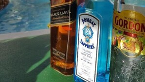 Tres botellas de alcohol sobre una mesa, con una piscina y un edificio al fondo.