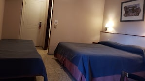 Habitación de hotel con dos camas, una puerta, un ventilador de techo, una lámpara fijada a la pared y un cuadro enmarcado.