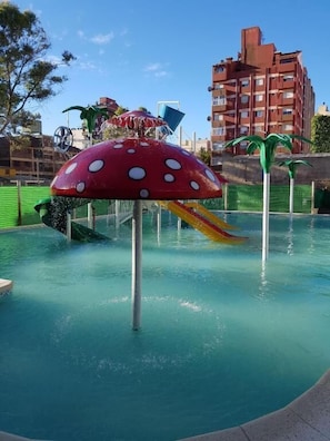 A water park with a mushroom-shaped slide and a building in the background. - HOTEL CHIAVARI (San Bernardo del Tuyú)
