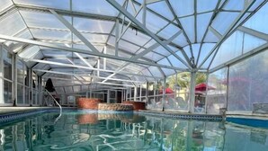 Una piscina con techo de cristal, rodeada por un muro de ladrillo y un cielo azul despejado.