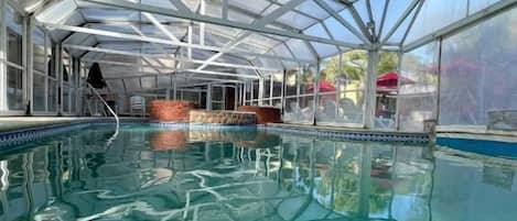 Una piscina con techo de cristal, rodeada por un muro de ladrillo y un cielo azul despejado.