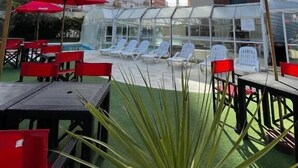 Un área de piscina en la azotea con sombrillas rojas, sillones de descanso y una estructura de cristal.