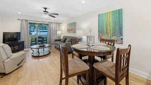 A living room with a TV, sofa, dining table, chairs, and artwork. - 🏖️Steps to Beach | Covered Patio | Seaside Beach and Raquet 2101🌴 (Orange Beach)