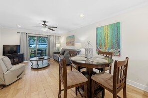 A living room with a TV, sofa, dining table, chairs, and artwork. - 🏖️Steps to Beach | Covered Patio | Seaside Beach and Raquet 2101🌴 (Orange Beach)