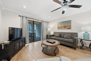 A modern living room with a flat-screen TV, a sofa, a coffee table, and a ceiling fan. - 🏖️Steps to Beach | Covered Patio | Seaside Beach and Raquet 2101🌴 (Orange Beach)