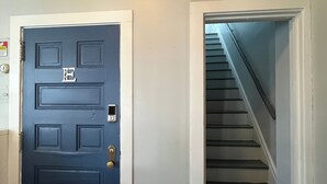 A blue door with a keypad lock, a stairwell with a handrail, and a white wall with a smoke detector.