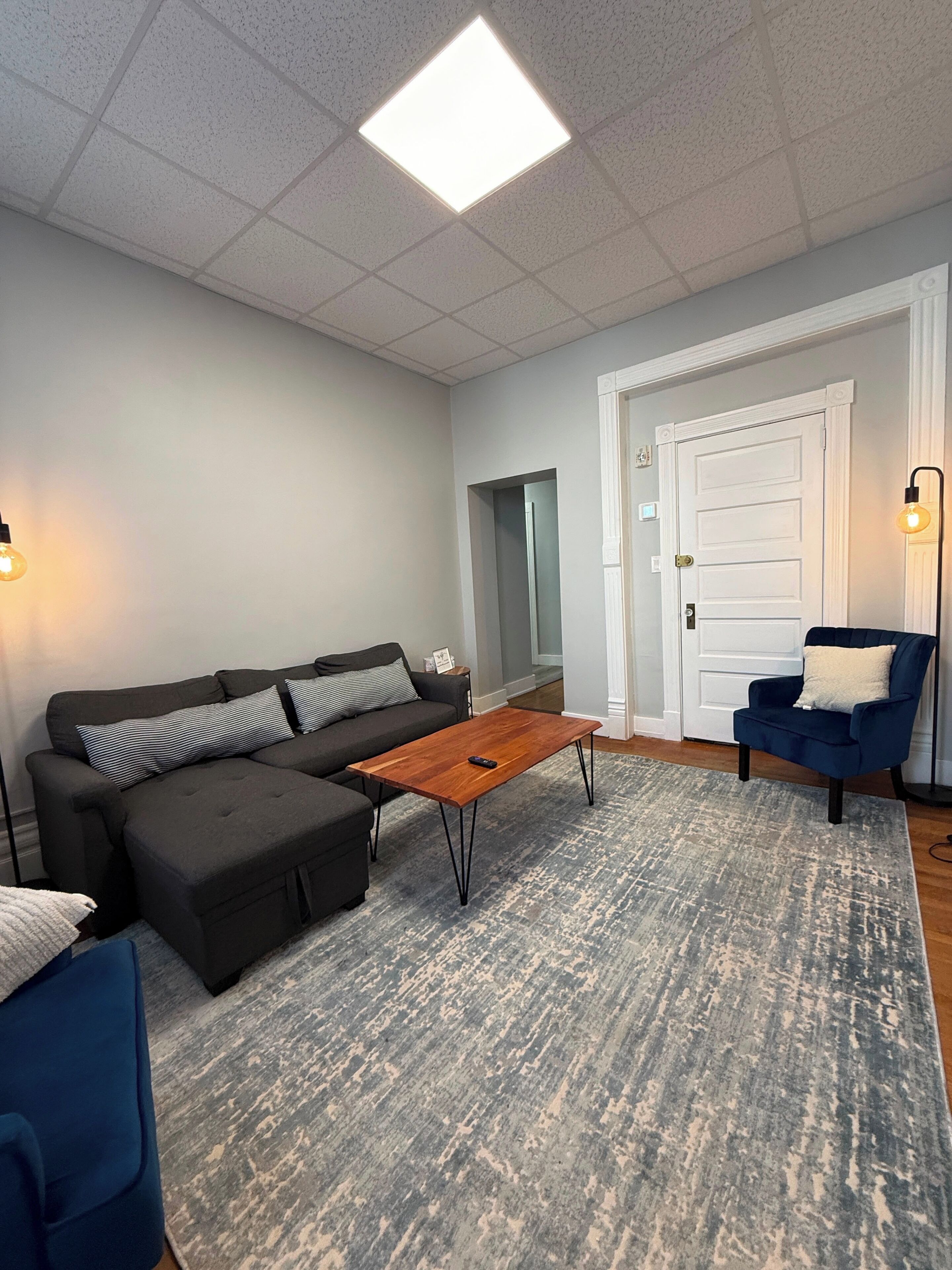 A living room with a sectional sofa, a coffee table, a blue armchair, and a patterned rug.