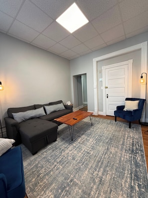 A living room with a sectional sofa, a coffee table, a blue armchair, and a patterned rug.