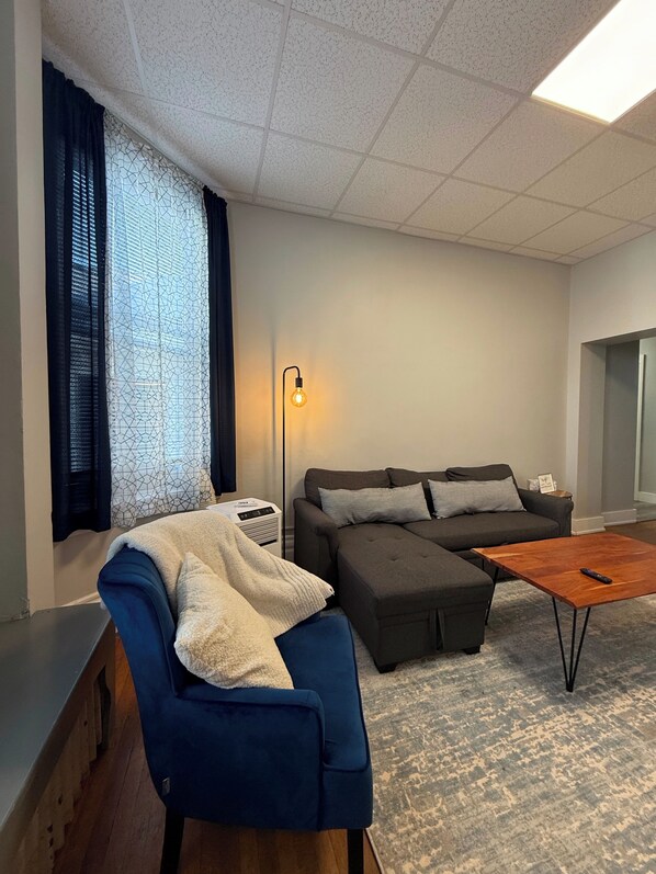 Una sala de estar moderna con un sofá modular, un sillón azul, una mesa de centro de madera y una lámpara de pie.