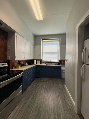 Cocina compacta con horno integrado, refrigerador y ventana con persianas.