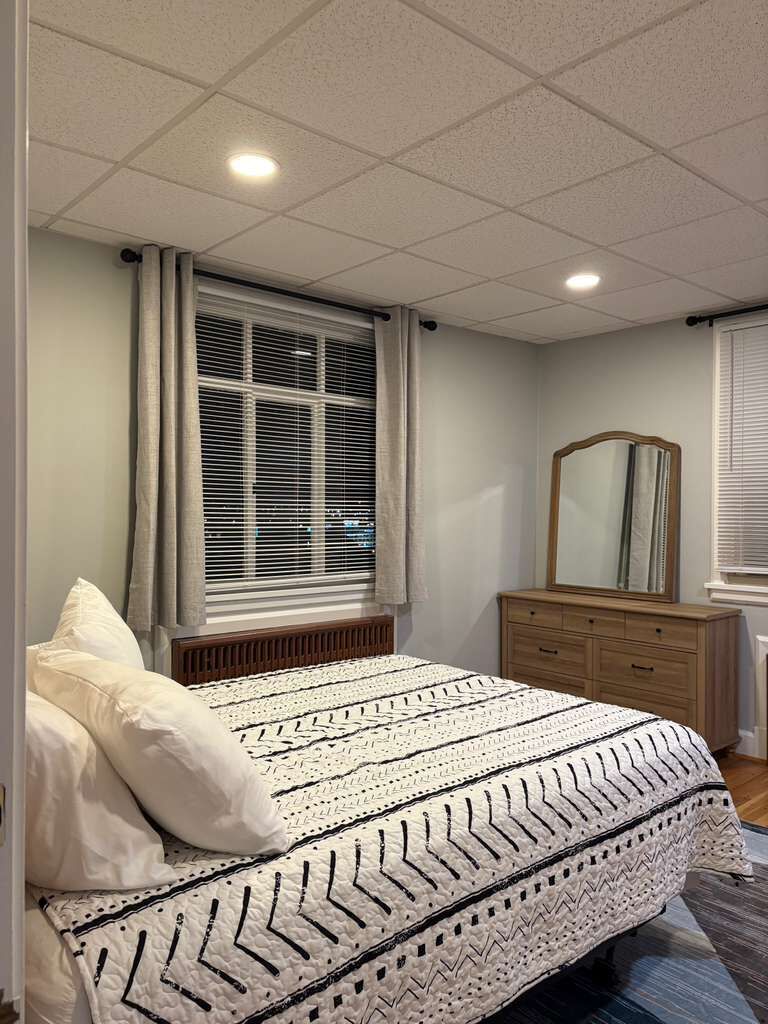 Une chambre à coucher avec un lit, une commode, un miroir et une fenêtre avec des stores.