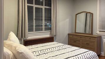 A bedroom with a bed, a dresser, a mirror, and a window with blinds.