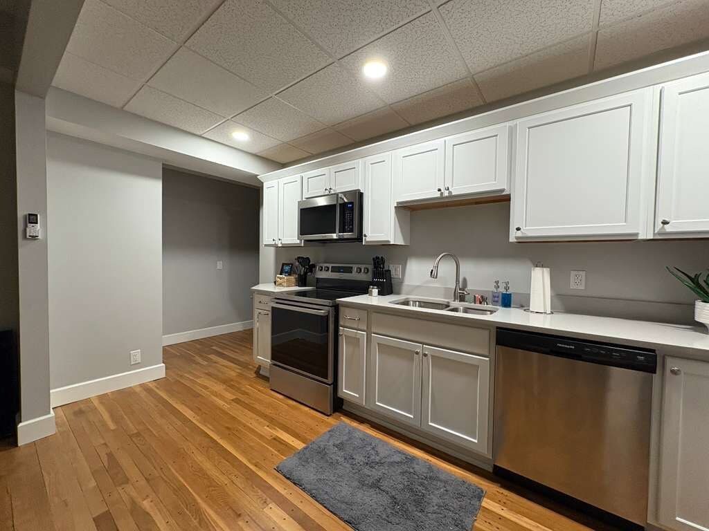 A modern kitchen with white cabinets, stainless steel appliances, and a grey rug.