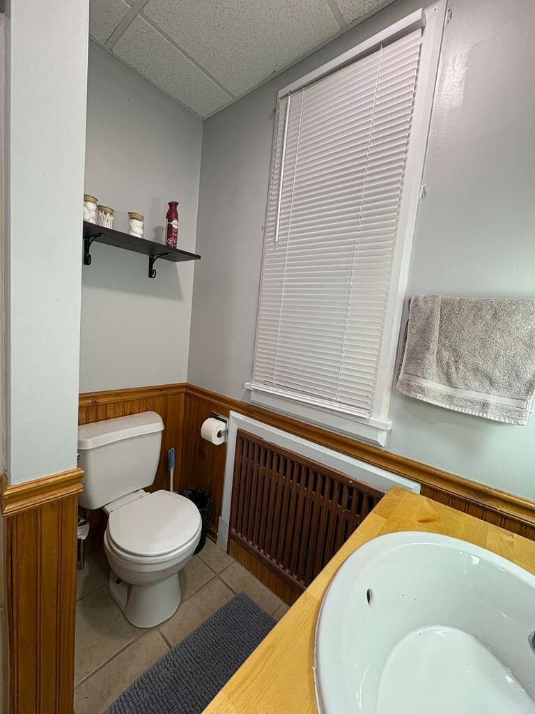 A bathroom with a toilet, a sink, a window with blinds, and a towel hanging on the wall.