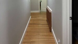 Un pasillo estrecho con piso de madera y paredes gris claro.