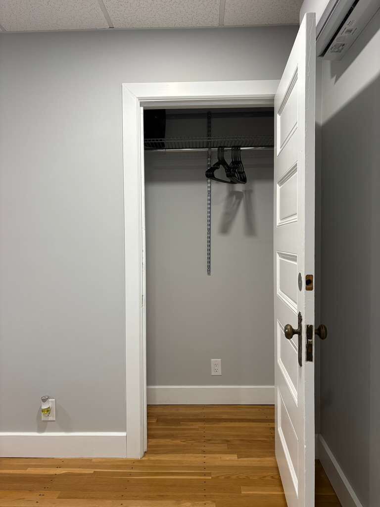 A room with a white door, a closet with hanging clothes, and a wooden floor.