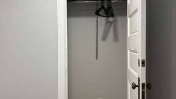 A room with a white door, a closet with hanging clothes, and a wooden floor.
