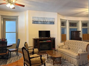 A living room with a fireplace, a television, a sofa, and a dining area with chairs and a table.