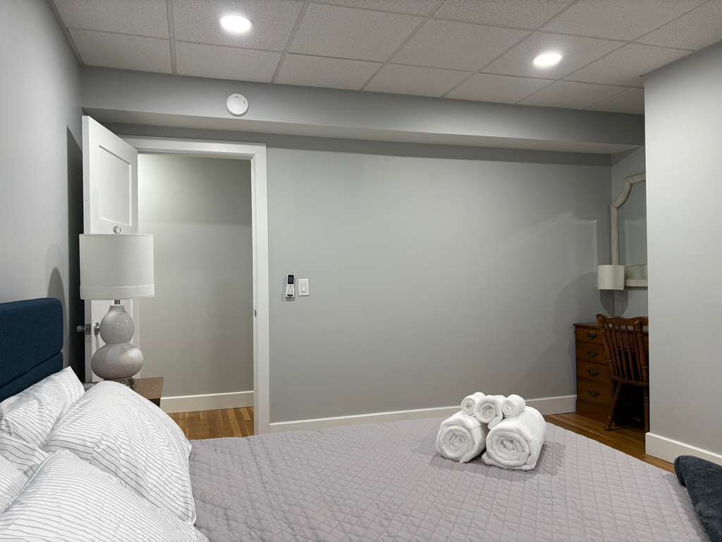 Quarto com cama, mesa de cabeceira, cômoda e porta que dá para outro espaço.