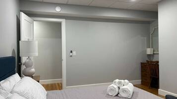 Quarto com cama, mesa de cabeceira, cômoda e porta que dá para outro espaço.