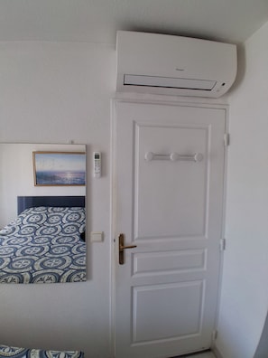 A room with a bed, a painting, a thermostat, and a door. - Air-conditioned 2-room apartment with a terrace, a 3-minute walk from the beach and restaurants (Cagnes-sur-Mer)