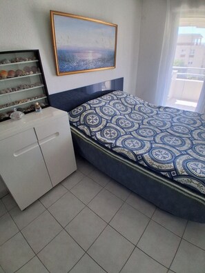 A bedroom with a bed, a dresser, a shelf with seashells, and a painting on the wall. - Air-conditioned 2-room apartment with a terrace, a 3-minute walk from the beach and restaurants (Cagnes-sur-Mer)
